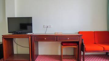 A wooden desk with a television, a red patterned rug, and a red sofa.