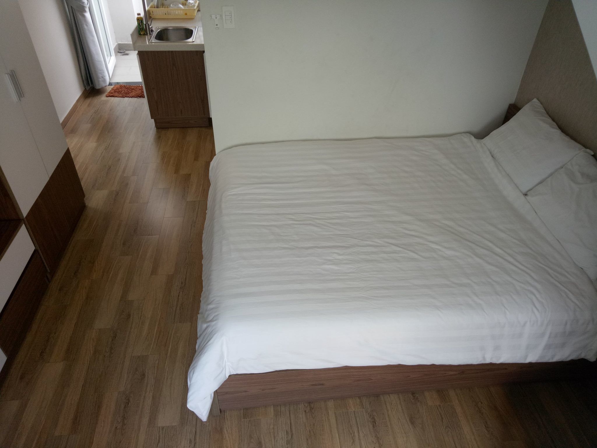 Une chambre avec un plancher en bois, un lit avec une literie blanche, une petite table de chevet en bois et une fenêtre avec des rideaux.