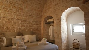 Ein Schlafzimmer mit Steinwänden, einem Bett, Kissen, einem kleinen Tisch und einem Korb.