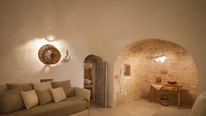 Ein gemütliches Wohnzimmer mit Steinwand, einem Holztisch mit Vase und Schale sowie einer Couch mit Kissen.