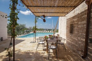 An outdoor patio with a pool, stone walls, and a table with chairs.