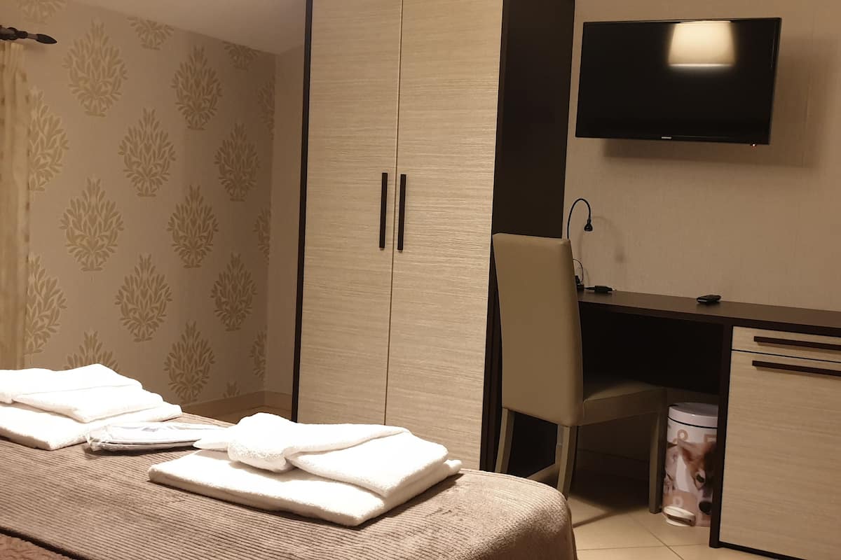 A hotel room with a bed, a desk, a TV, and a wardrobe.