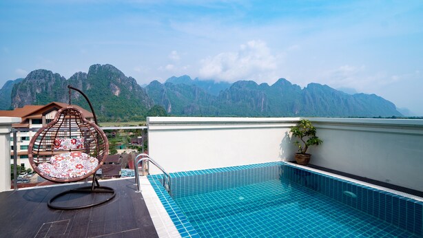 Une piscine sur le toit avec vue sur les montagnes, un fauteuil suspendu et une plante en pot.