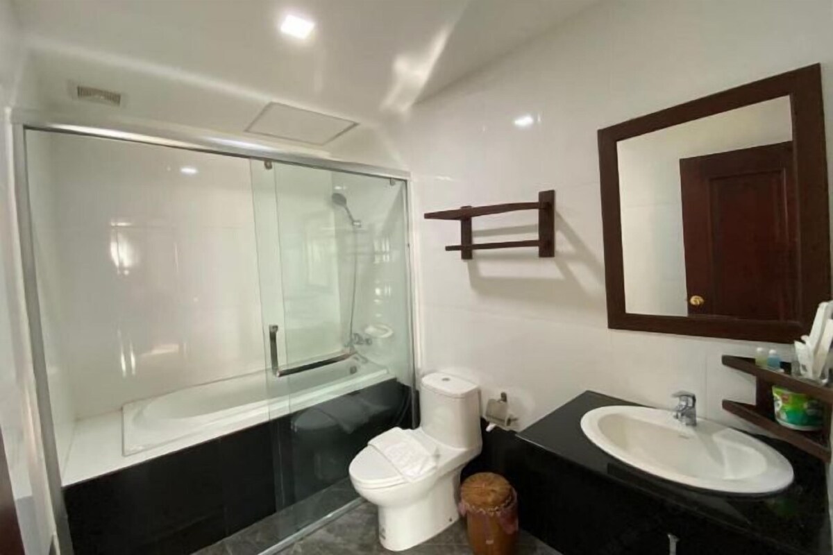 A modern bathroom with a glass-enclosed shower, a white toilet, a black sink, and a wooden-framed mirror.