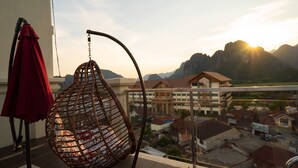 Un fauteuil suspendu avec un coussin à motifs, placé sur un balcon donnant sur un paysage montagneux.