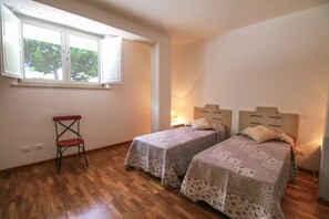 Un dormitorio con dos camas individuales, suelo de madera, una ventana y una silla.