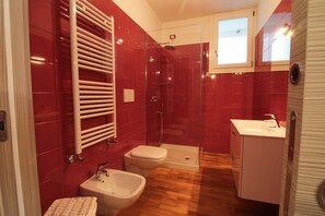 Un baño con baldosas rojas, cabina de ducha de vidrio, un bidé, un lavabo y un armario.