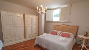 A bedroom with a large bed, a chandelier, a window, and built-in wardrobes.