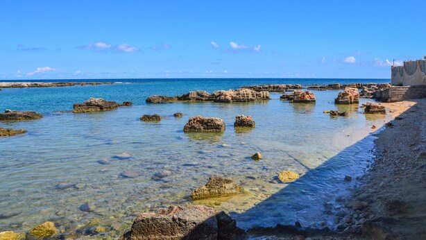 A coastal scene with clear water, rocky formations, and a building on the right.
