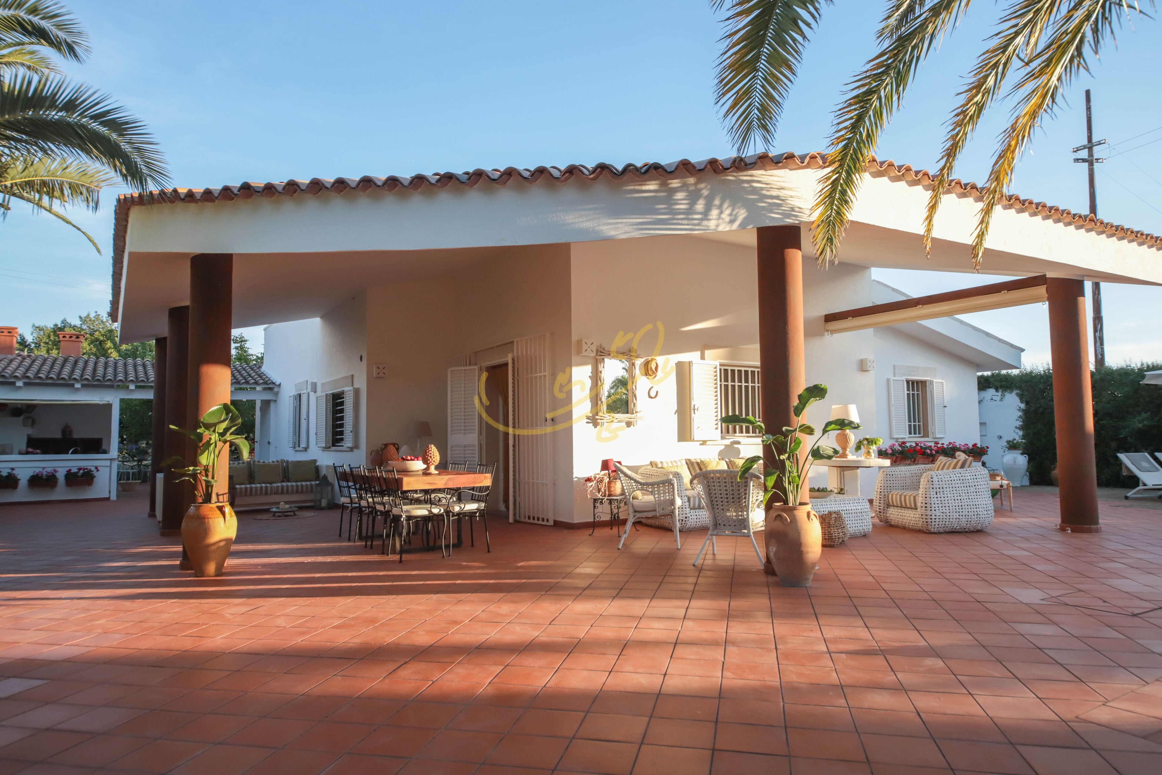 An outdoor patio area with a covered seating area, a dining table, and potted plants.