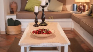 Una sala de estar acogedora con una mesa de centro blanca, un cuenco de bayas rojas, dos velas y un sofá con cojines.