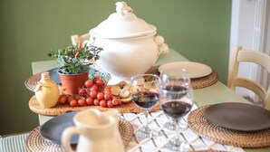 Una mesa de comedor dispuesta con una olla blanca grande, una planta en maceta, una jarrón y una copa de vino tinto.