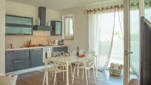 A modern kitchen with grey cabinets, a dining table with white chairs, and a window with sheer curtains. - TD Villa Patrizia Pool & Alfresco Kitchen (Monopoli)