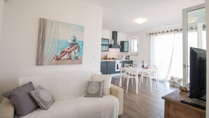 A modern living room with a white sofa, a dining area with a white table and chairs, a kitchen with dark cabinets, and a large window with curtains. - TD Villa Patrizia Pool & Alfresco Kitchen (Monopoli)
