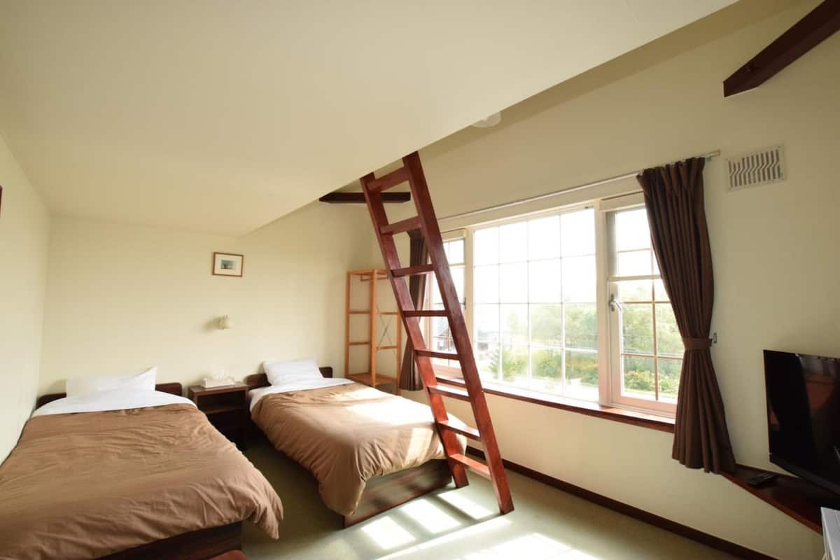 A room with two beds, a TV, and a window with curtains.