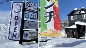 A snow-covered outdoor area with a sign for a restaurant and a banner with Japanese text. - Niseko OAC Lodge (Niseko)
