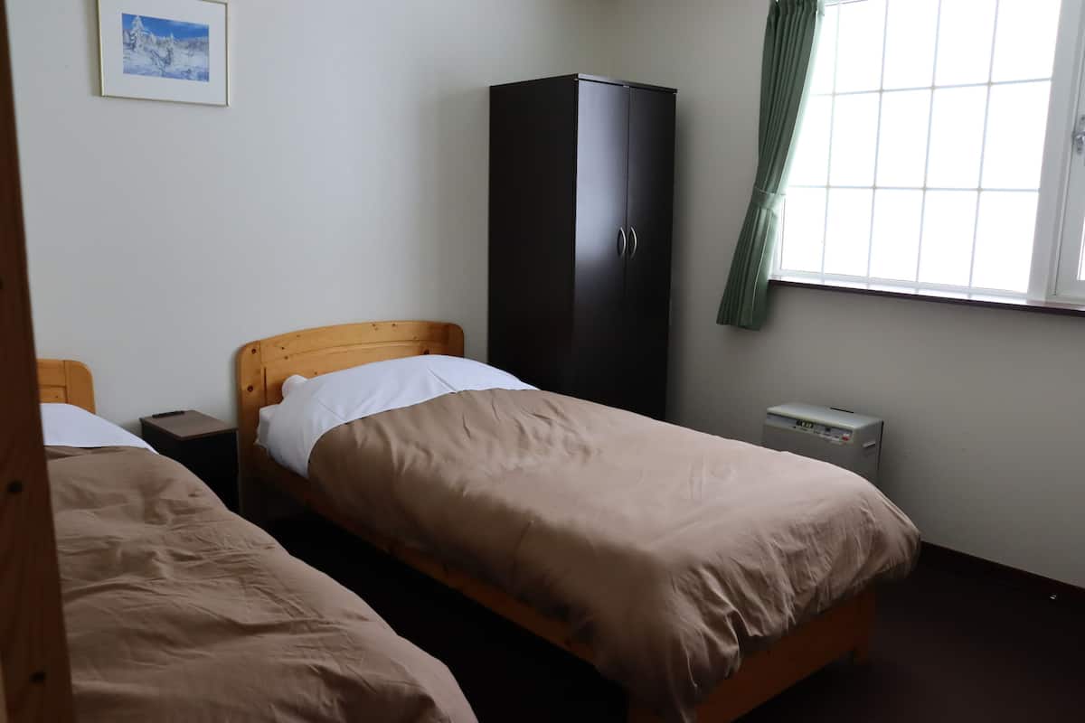 A bedroom with two single beds, a wardrobe, a bedside table, a nightstand, and a window with curtains.
