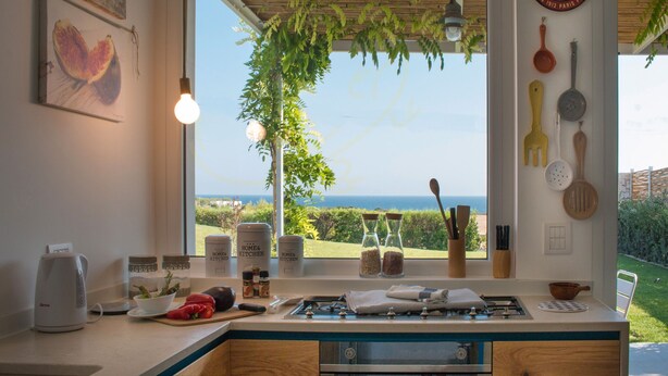 Una cocina con vista al mar, techo de madera y diversos utensilios de cocina en la pared.