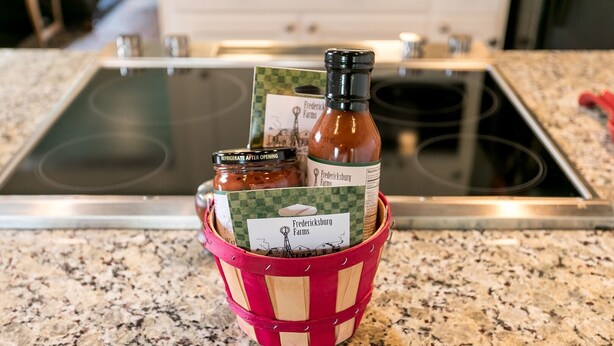 Una encimera de cocina con una cesta roja de tejido que contiene dos tarros de vidrio y una tarjeta de Frederick Farms.