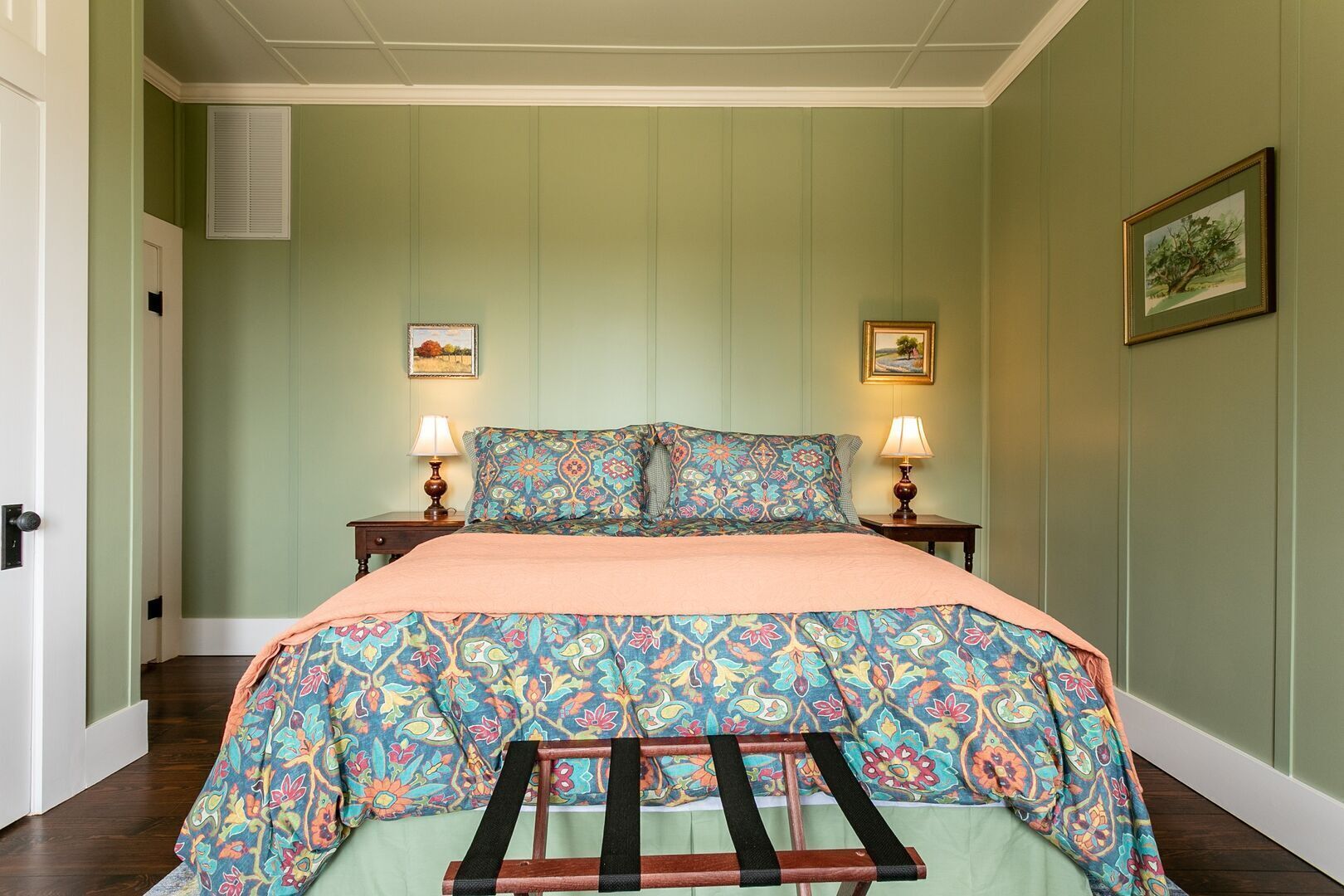 Une chambre à coucher avec un lit, deux tables de chevet, deux lampes et deux tableaux encadrés accrochés au mur.