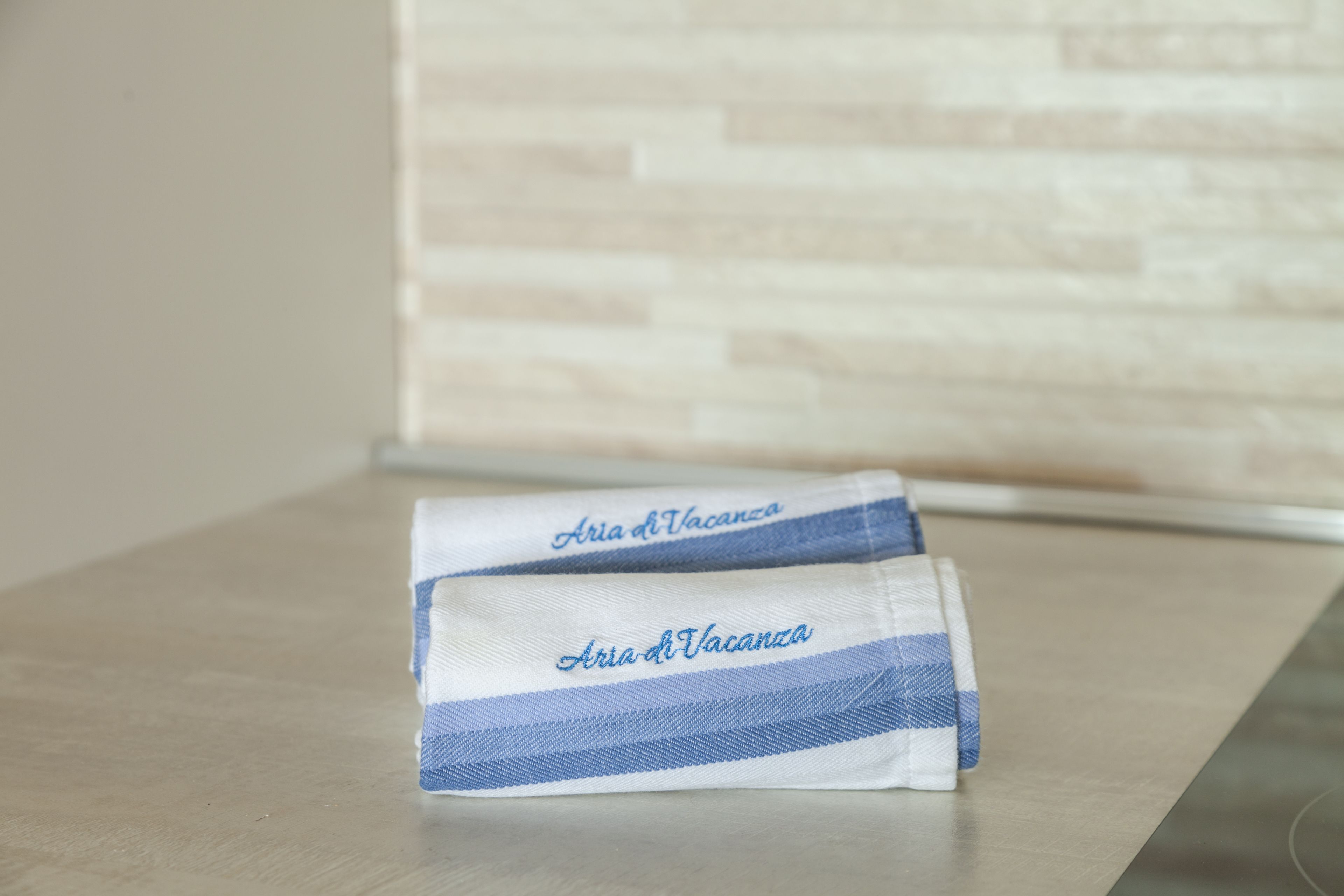 Deux serviettes pliées, avec l’inscription « Aria di Vacanza » sur une surface métallique.