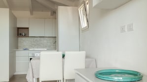 A modern kitchen with white cabinetry, a dining area with white chairs, and a teal glass bowl on the counter. - Aria di Vacanza - Azalee (Olbia)