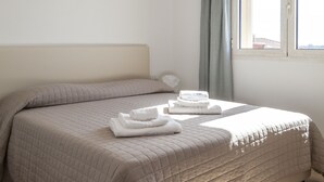 A bedroom with a large bed, a window with curtains, and a white ceiling. - Aria di Vacanza - Azalee (Olbia)