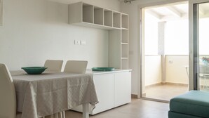 A dining area with a table, chairs, and a green bowl. There is a white cabinet above the table and a sliding glass door leading to a balcony. - Aria di Vacanza - Azalee (Olbia)