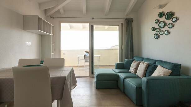 A living room with a green sofa, a dining table with chairs, and a balcony with a table and chairs. - Aria di Vacanza - Azalee (Olbia)