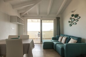 A living room with a green sofa, a dining table with chairs, and a balcony with a table and chairs. - Aria di Vacanza - Azalee (Olbia)