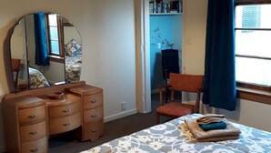 A bedroom with a bed, a dresser, a chair, a mirror, and a window with curtains.