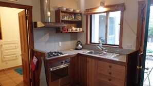 A compact kitchen with wooden cabinets, a gas stove, a built-in oven, a stainless steel sink, and a window with a view of the outside.