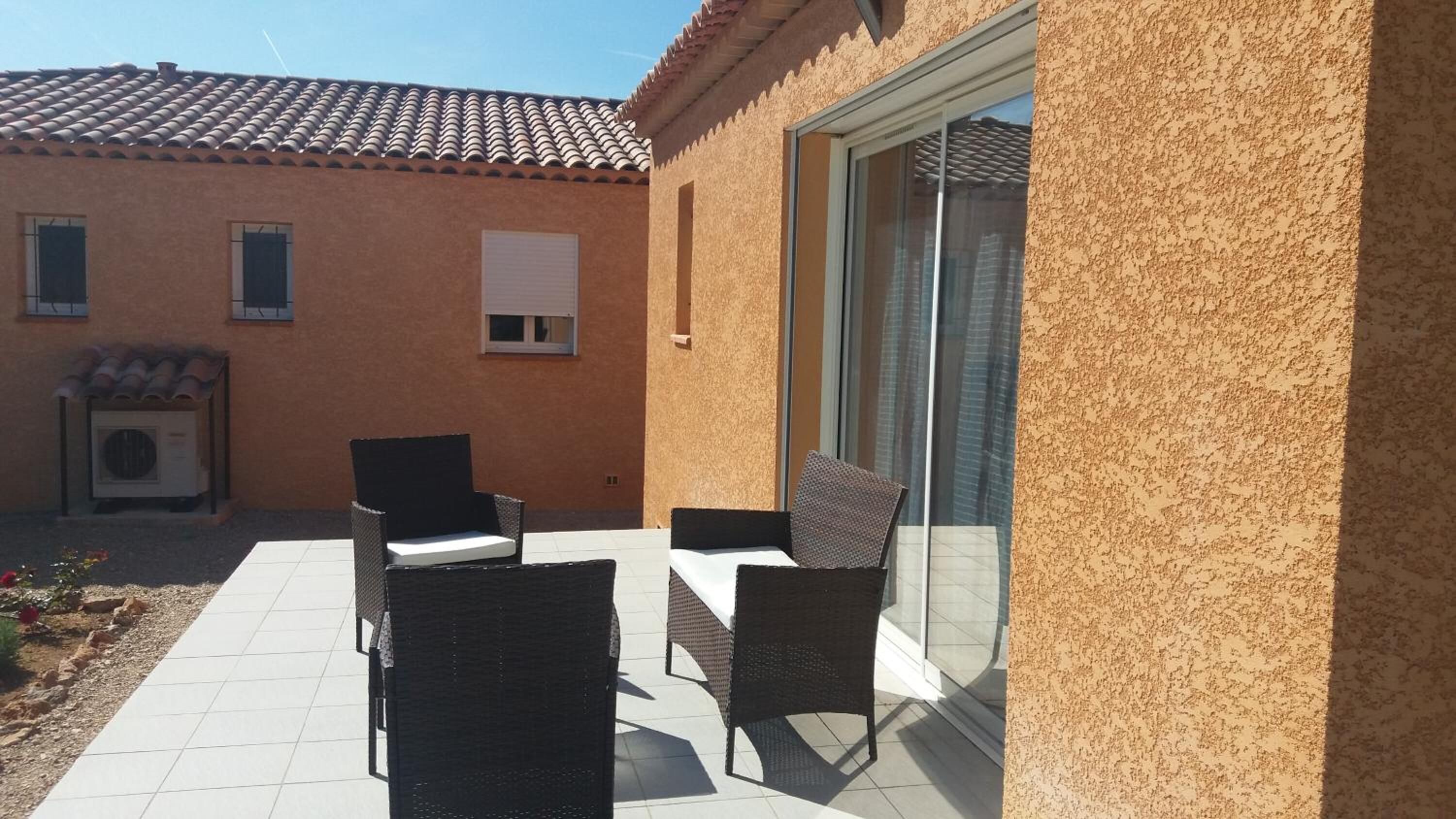 Un patio con dos sillas de mimbre, una mesa, una puerta corrediza de vidrio y un techo de baldosas.