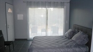 Een slaapkamer met een bed, een stoel, een deur en een raam met gordijnen.