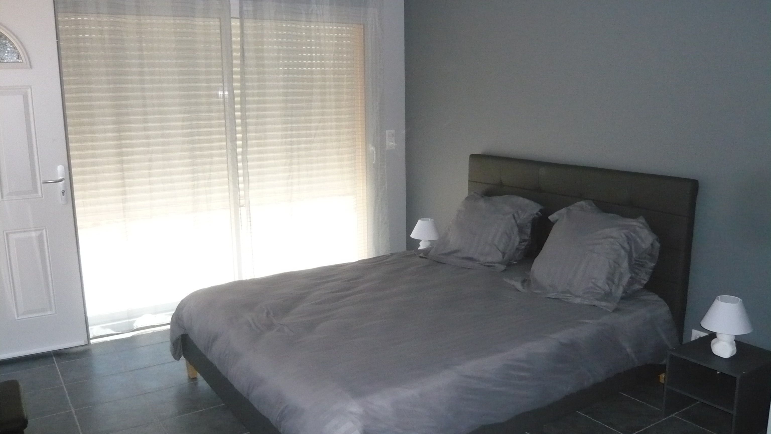 Un dormitorio con cama, dos lámparas de noche, una puerta y una ventana con persianas.