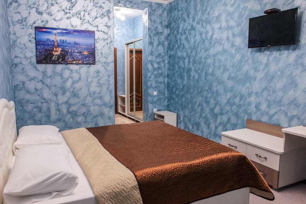 Un dormitorio con cama, mesita de noche, cómoda, televisor montado en la pared y espejo.