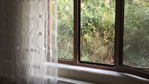 Quarto com cama, radiador e janela com vista para o verde.