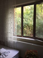 A room with a bed, a radiator, and a window with a view of greenery.