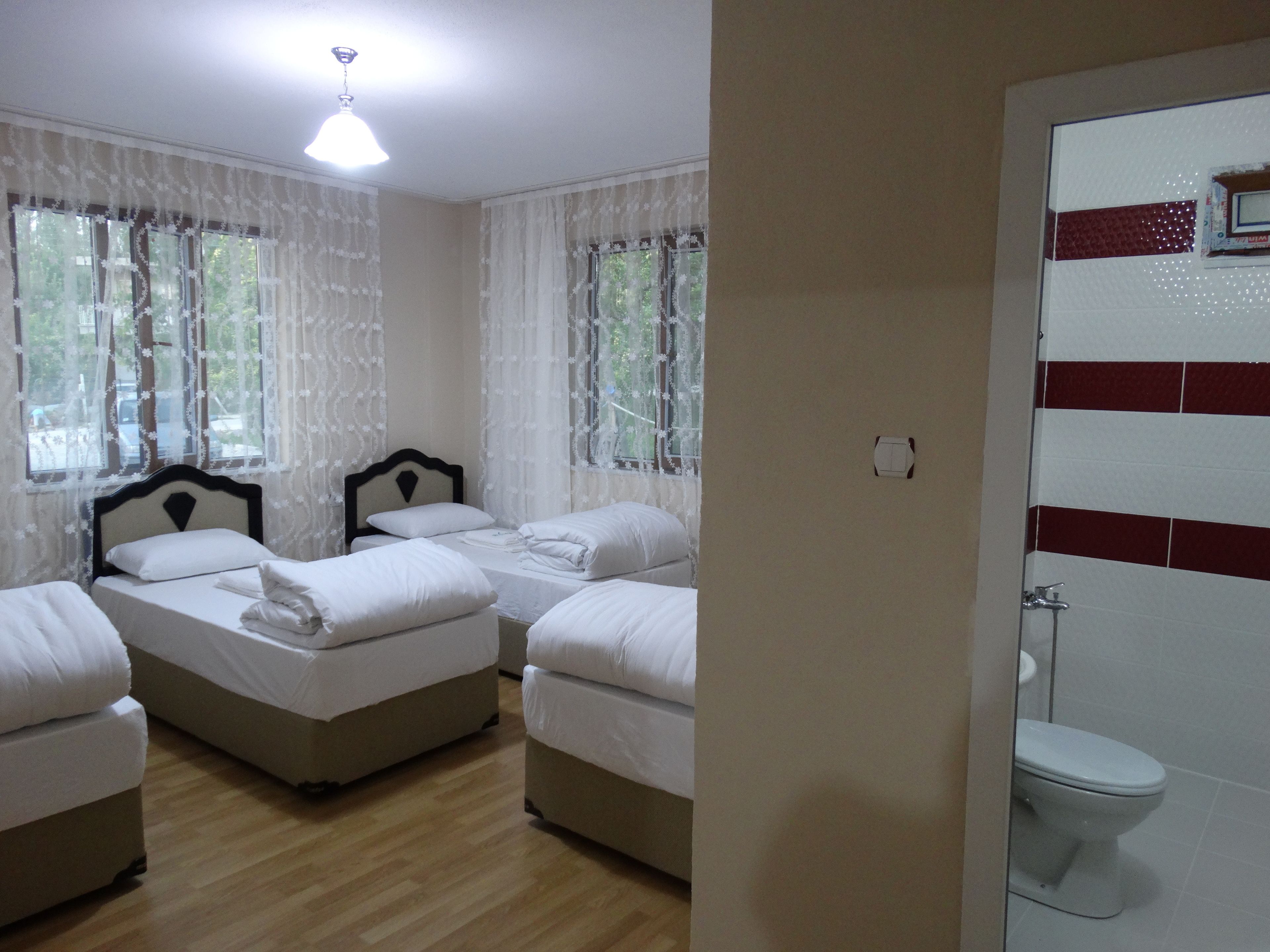 Habitación de hotel con dos camas, piso de madera, ventana con cortinas de encaje y vista al exterior.