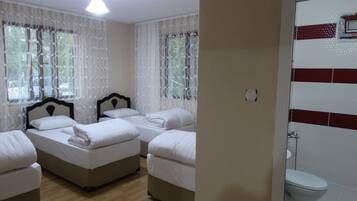 Habitación de hotel con dos camas, piso de madera, ventana con cortinas de encaje y vista al exterior.