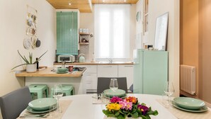 Une cuisine moderne avec un coin repas, dotée d’un plafond en bois, de meubles de couleur verte et d’une fenêtre avec des rideaux.