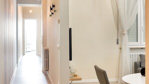 Un couloir avec un plancher en bois, une porte blanche au fond et un objet noir accroché au mur.