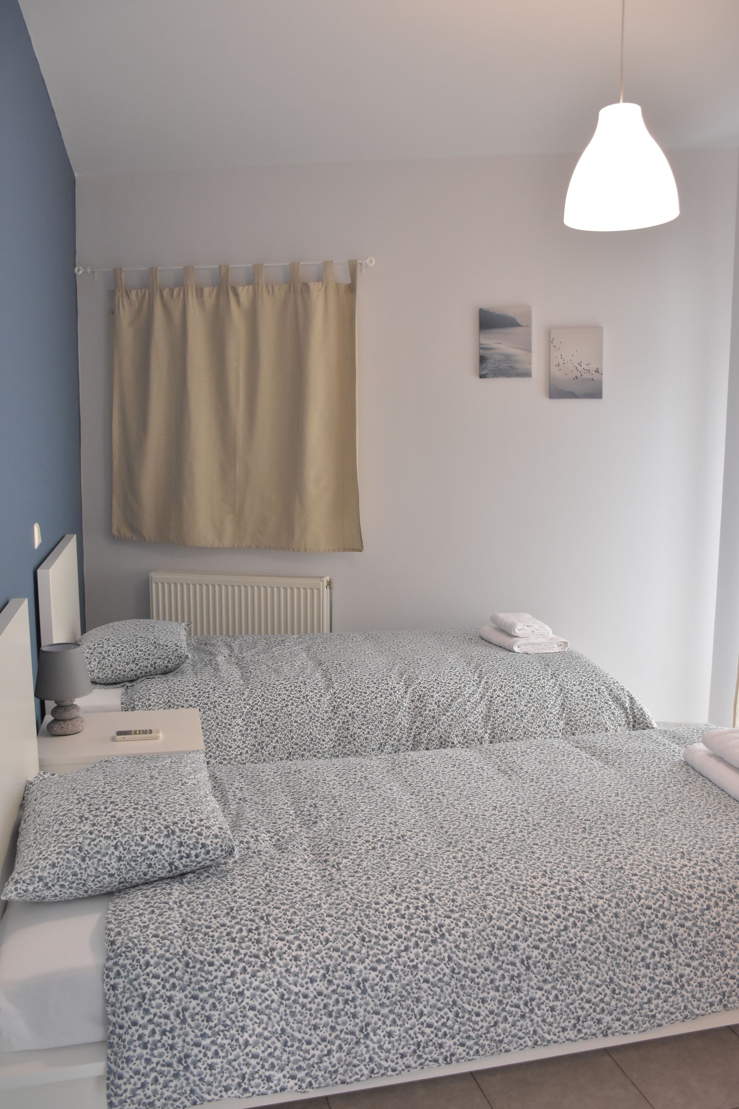 Un dormitorio con cama, mesita de noche, lámpara y ventana con cortinas.