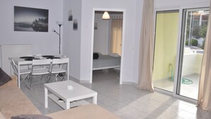 Ein modernes Wohnzimmer mit einem weißen Sofa, einem Esstisch mit Stühlen, einem kleinen weißen Tisch und einem Bett im Hintergrund.