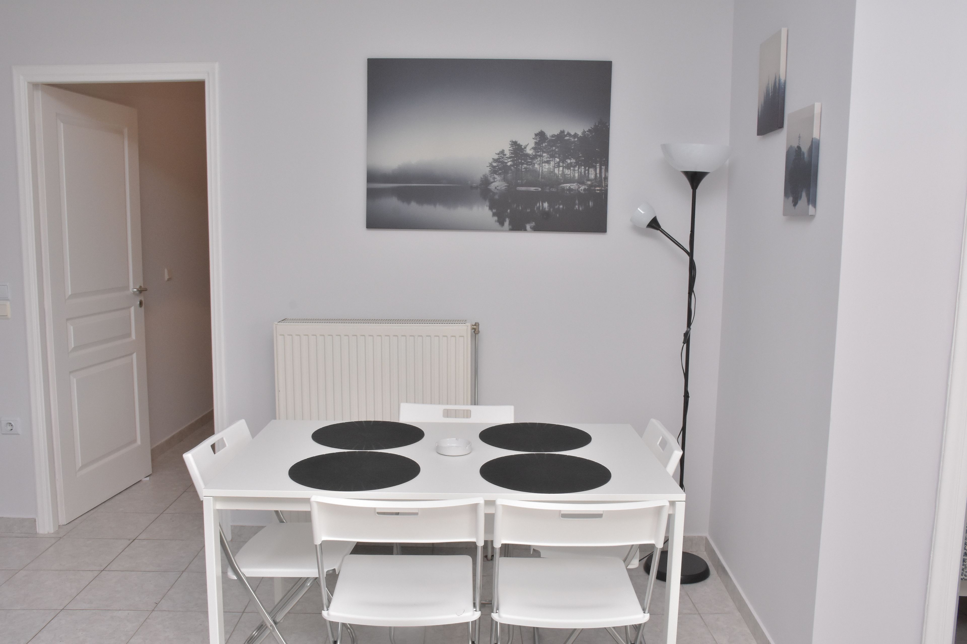 A dining area with a white table and chairs, a black and white painting on the wall, and a floor lamp.