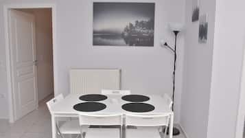 A dining area with a white table and chairs, a black and white painting on the wall, and a floor lamp.
