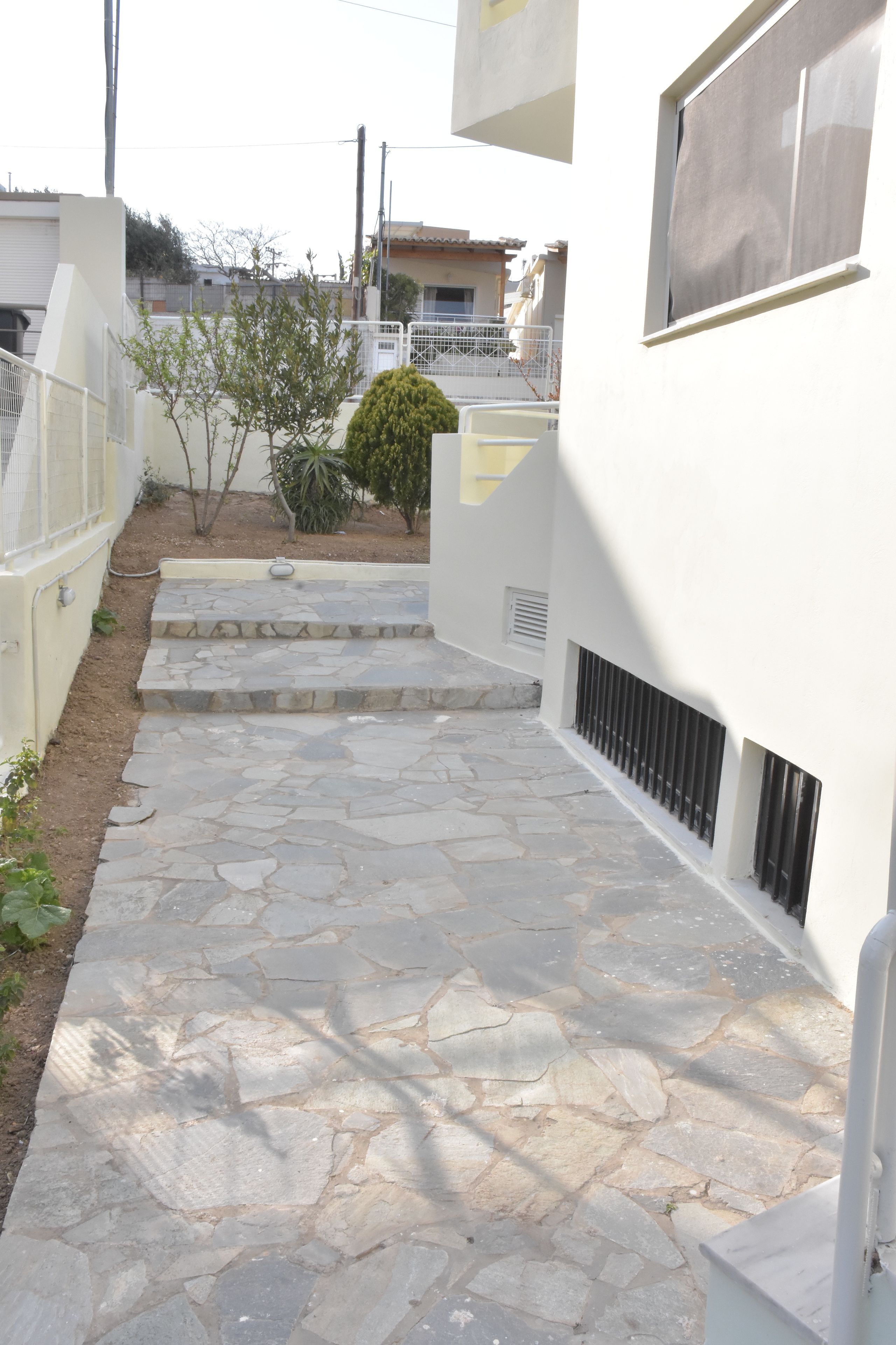 A stone-paved pathway leading to a white building with a small garden and steps.