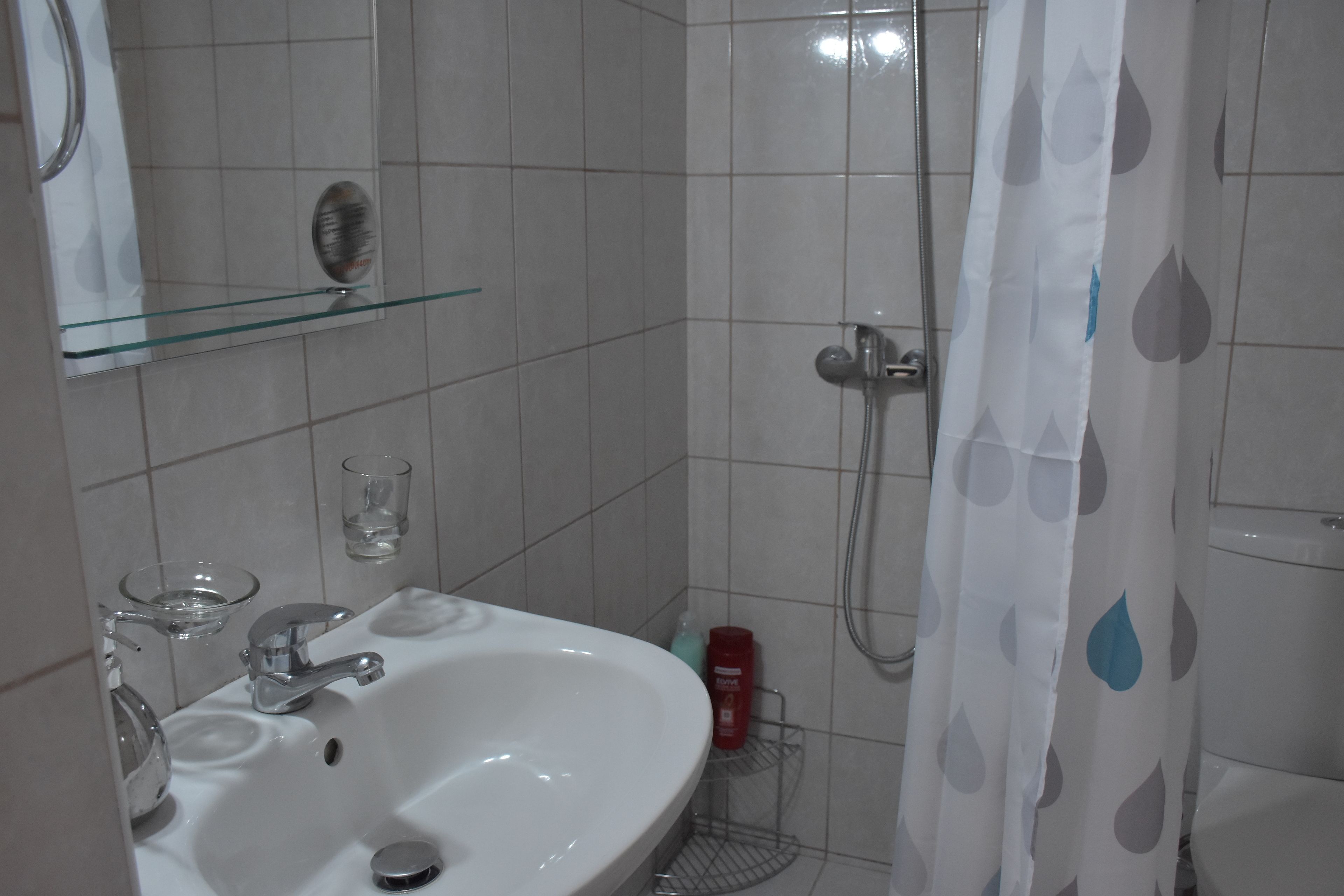 Casa de banho com lavatório branco, espelho e cortina de chuveiro.