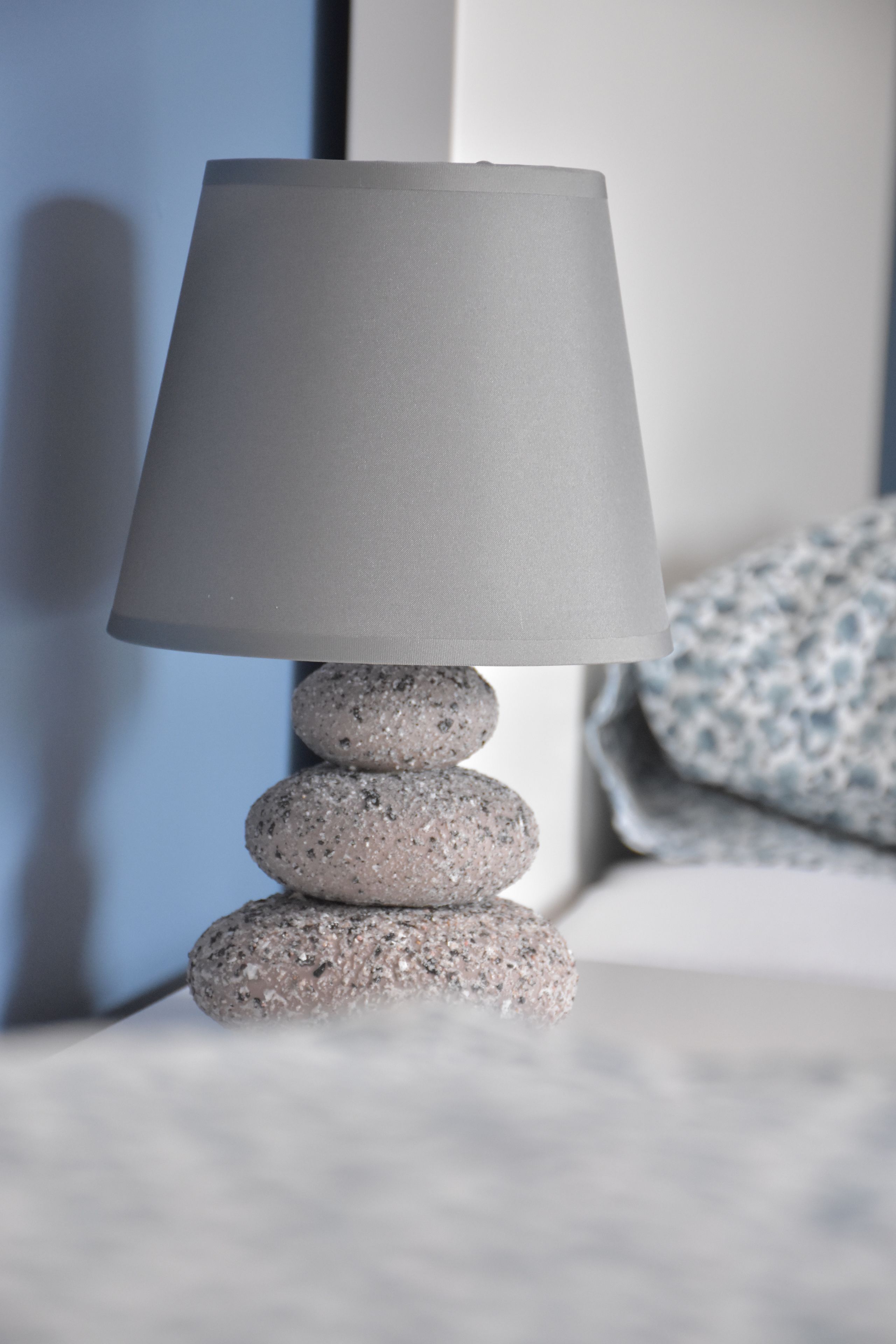 A lamp with a grey shade on a stack of grey stones.