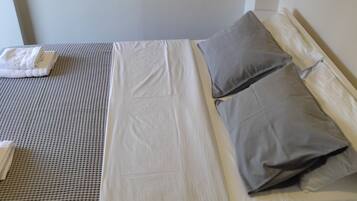 Een eenpersoonsbed met wit en grijs beddengoed, een klein nachtkastje met een opgevouwen witte handdoek, en een ingelijst foto aan de muur.